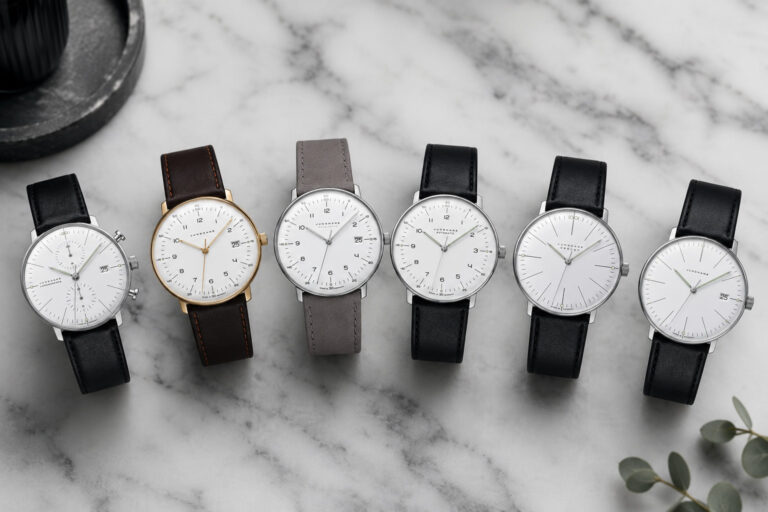 Six minimalist analog watches with white dials and leather straps lined up on a marble surface for a product shot