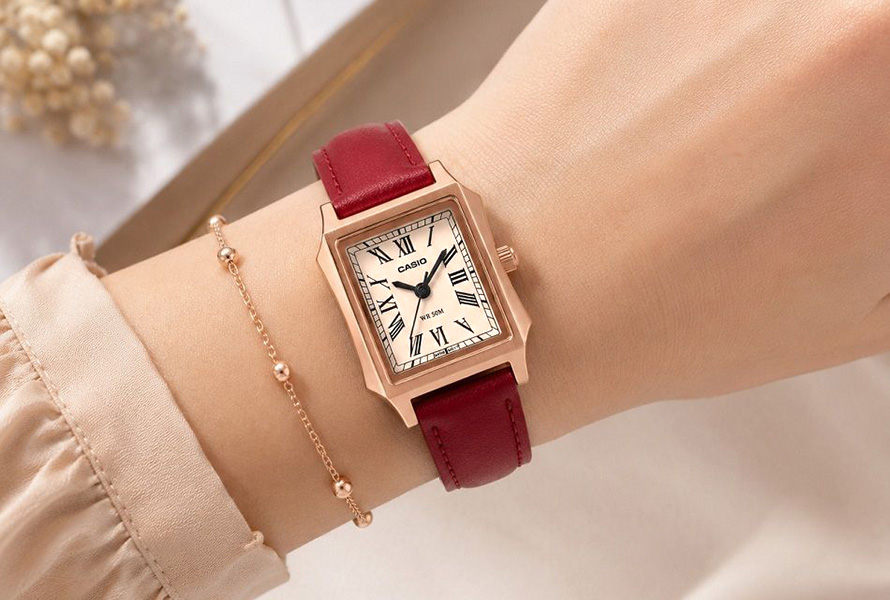 Casio Tank LTP-B190RGL-4BVER ⌚ Schweizer Uhren Magazin Wrist wearing a rose‑gold rectangular Casio watch with a burgundy leather strap, paired with a delicate gold bracelet.